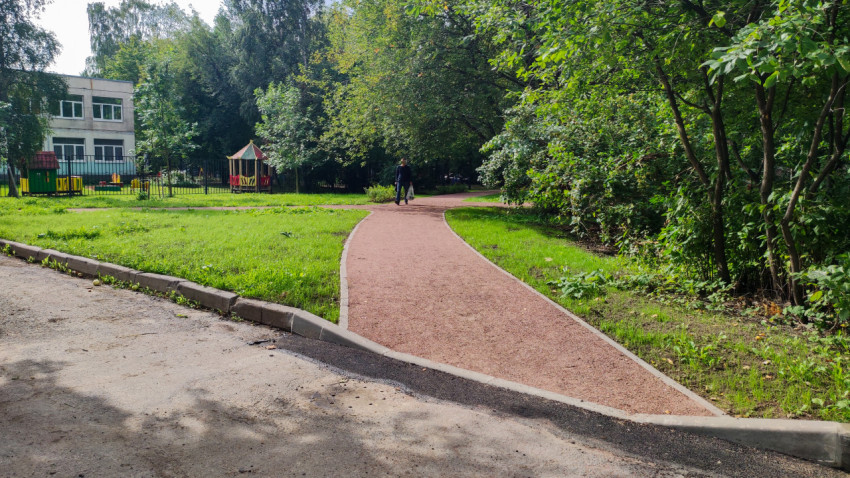 По красной дорожке идёт человек, а за забором видна детская площадка и здание среди деревьев
