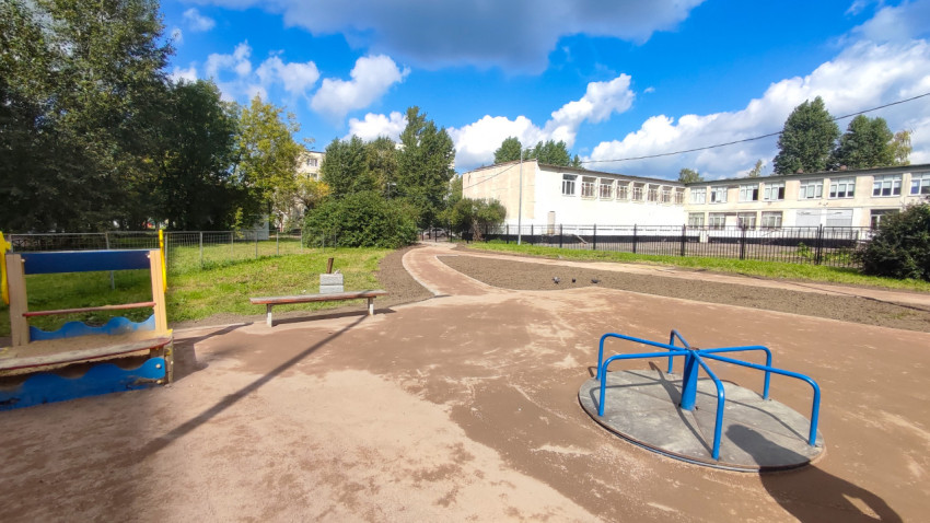 Площадка с каруселью и игровыми зонами рядом со зданием учреждения за ограждением