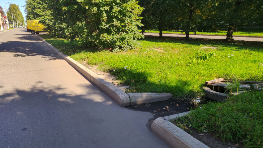 Бордюрный съезд к водоотводной канаве у асфальтовой дороги рядом с зелёным газоном