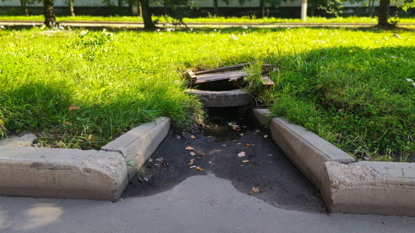 Водоотводная канава с бетонным кольцом и деревянным настилом у края тротуара и бордюров