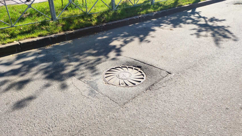 Канализационный люк на асфальтовой дороге у бордюра и газона