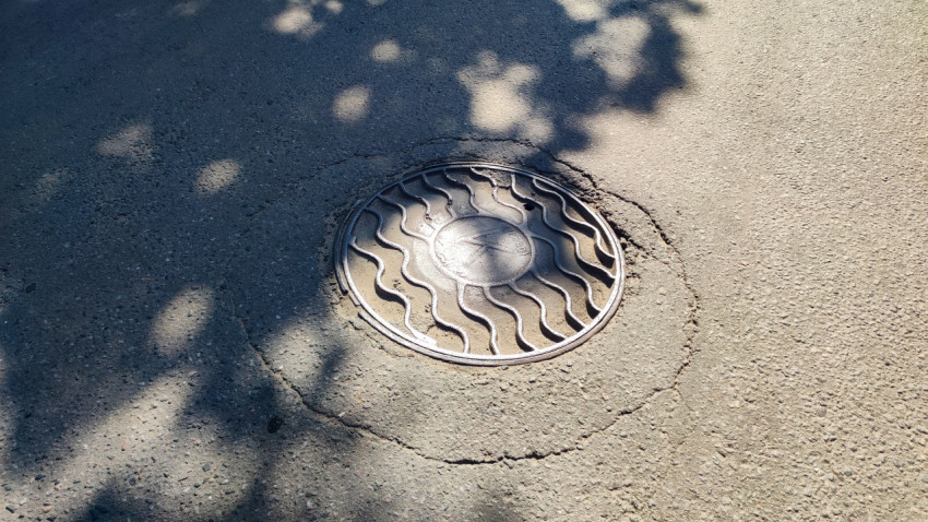 Чугунный люк колодца с рельефным узором в асфальтовом покрытии дороги