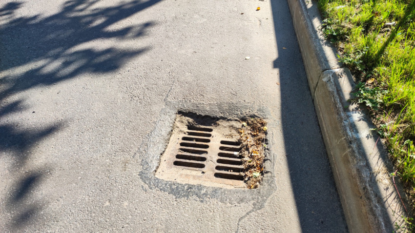 Дождеприёмная решётка у бордюра, вокруг листья и влажная обочина
