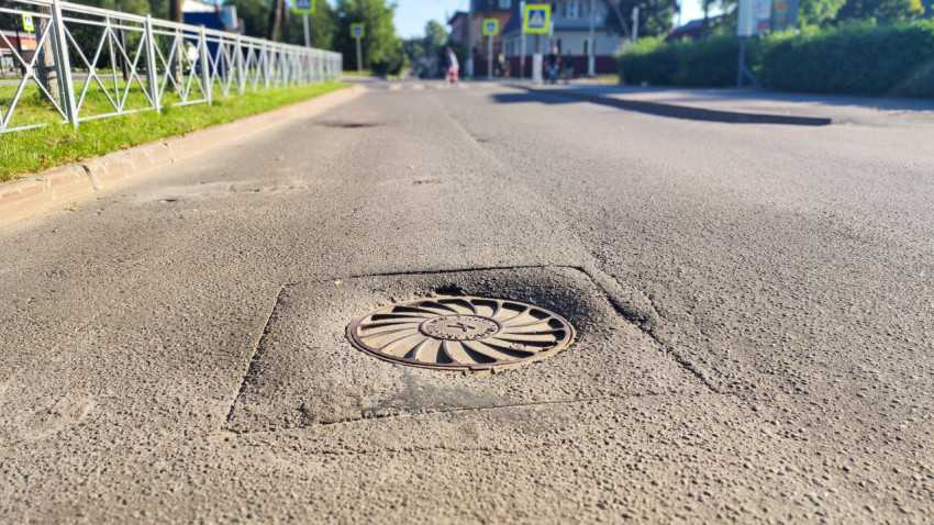 Люк колодца в квадратной заплатке асфальта снят крупным планом с уровня дороги