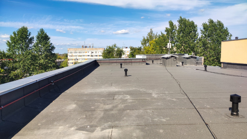 Панорама плоской кровли с вентиляционными выходами и кабельными линиями среди деревьев