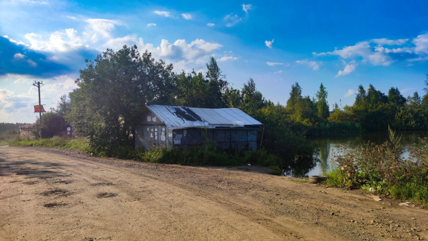 Грунтовая дорога с лужами у пруда и небольшого металлического строения
