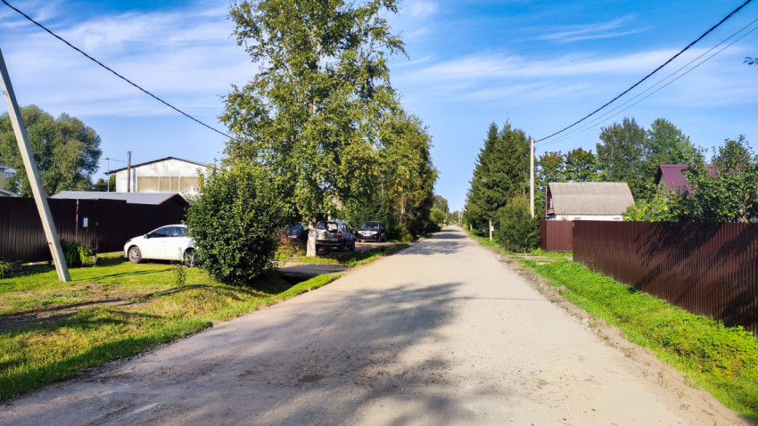 Грунтовая дорога в частном секторе с заборами, деревьями и воздушными линиями электропередачи