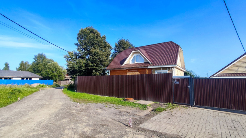 Грунтовая улица у металлического забора с частным домом и разметочными колышками