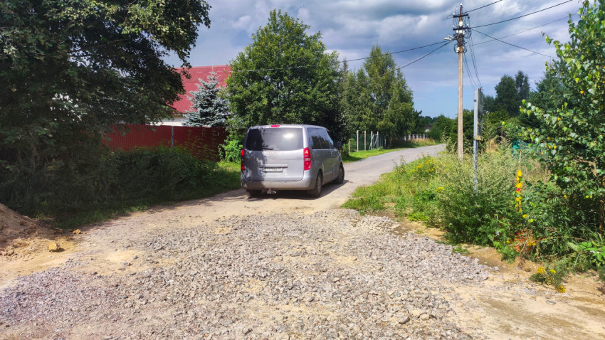 Участок дороги с отсыпкой щебнем и припаркованным фургоном у частных домов