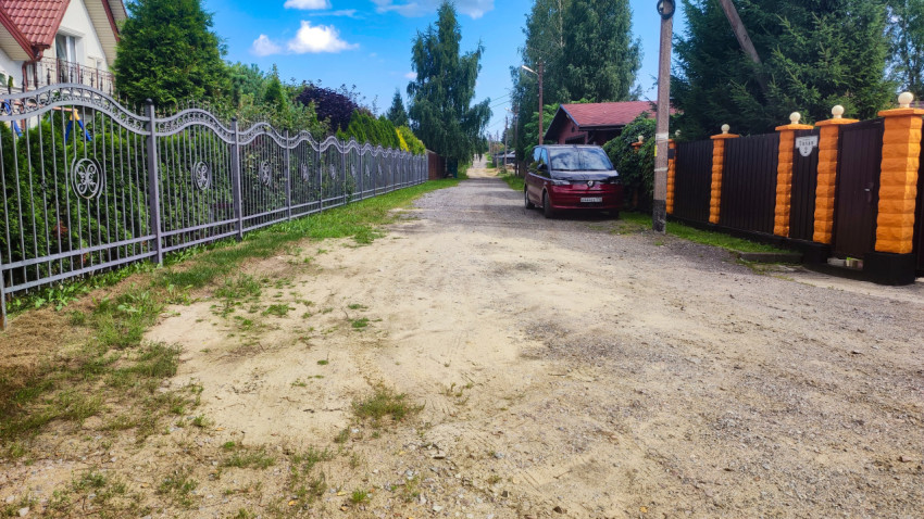 Узкая улица в коттеджном посёлке с металлическими заборами и припаркованным автомобилем