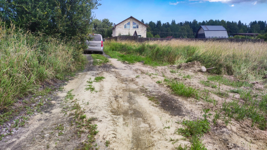 Песчаная грунтовая колея к частным домам среди высокой травы и поля