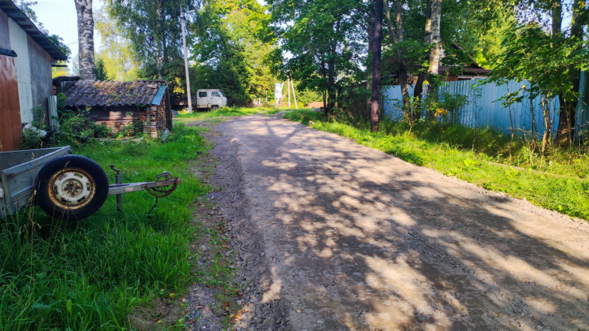 Грунтово-щебёночная дорога у заборов с прицепом и хозяйственными постройками