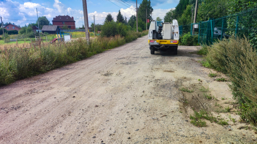 Дорожно-строительная машина на просёлочной дороге рядом с детской площадкой и частными домами