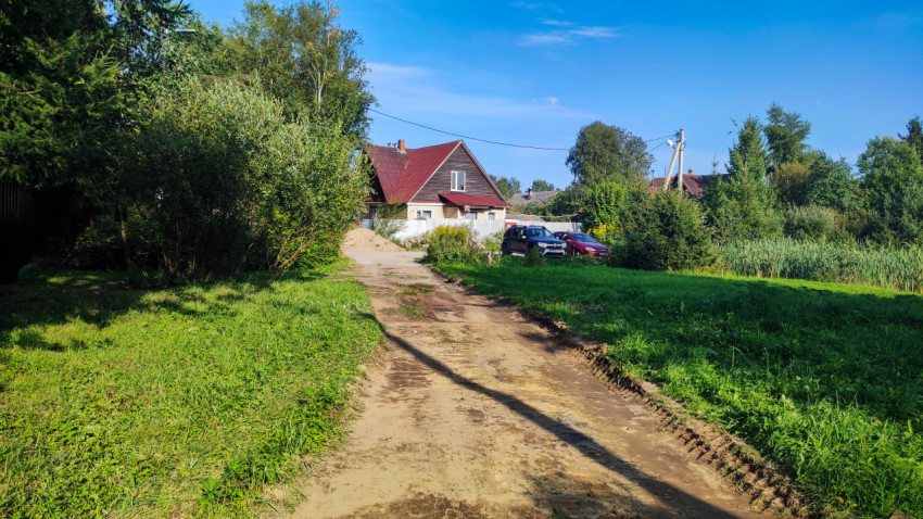 Грунтовая улица в частном секторе с забором, домами и линией электропередачи