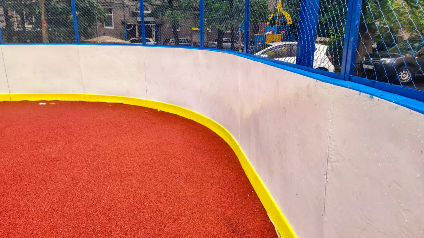 Угол спортивной коробки с закруглёнными бортами и красным резиновым покрытием после дождя