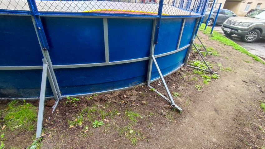 Металлические подпорки и синий борт спортивной площадки во дворе