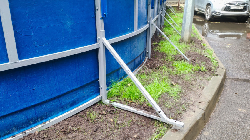 Металлическая подпорка ограждения у бордюра на мокрой улице