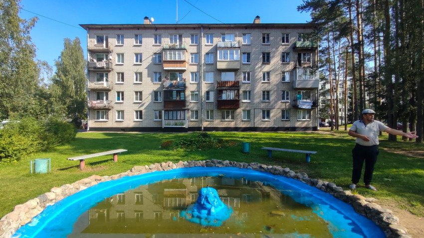 Декоративный фонтан во дворе на фоне жилых домов и зелёной зоны