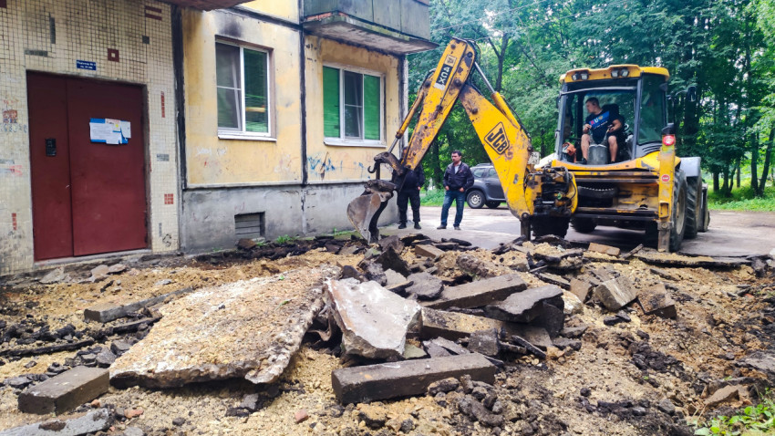 Экскаватор разрушает асфальт у подъезда жилого дома