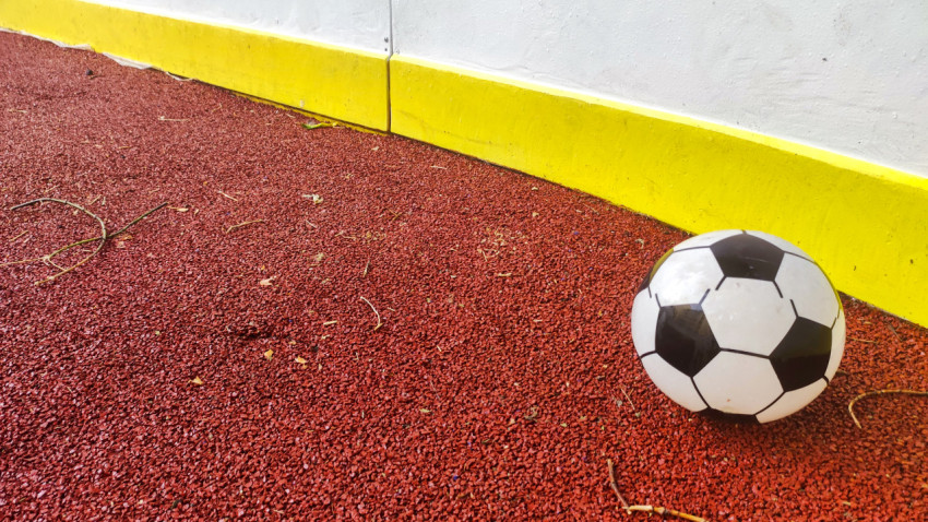 Футбольный мяч на резиновом покрытии рядом с желтым отбойником