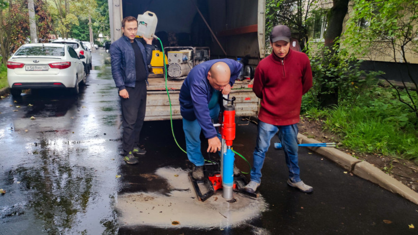 Оператор с канистрой и установка для кернения асфальта на мокрой дороге рядом с техникой