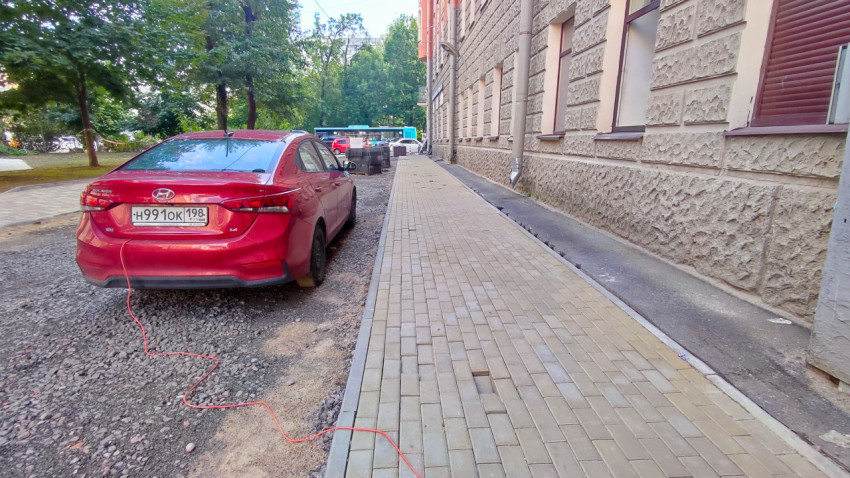 Красный автомобиль Hyundai Solaris у нового тротуара из плитки вдоль фасада здания