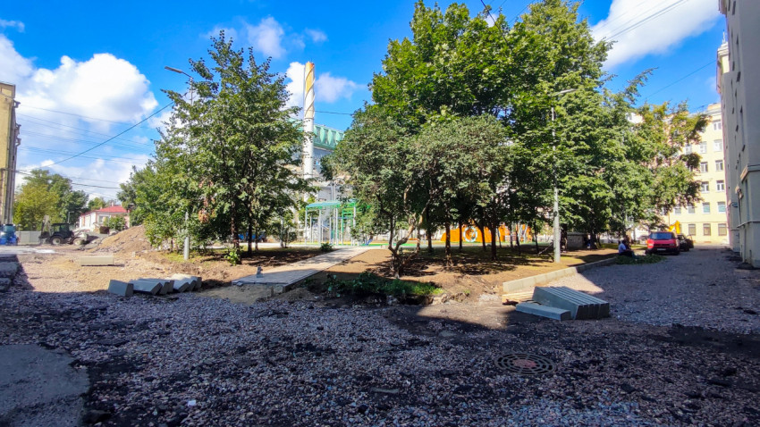 Двор с деревьями и строительным щебнем при укладке дорожек и установке бордюров