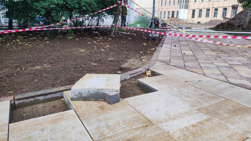 Незавершенная укладка тротуарной плитки у бордюра на огражденной строительной зоне