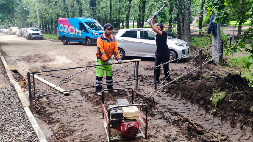 Рабочие с кувалдой и виброплитой устанавливают опоры ограждения при благоустройстве двора