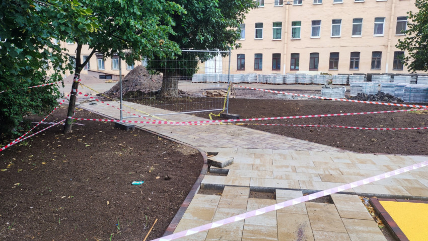 Огражденный участок благоустройства с укладкой тротуарной плитки и паллетами материалов