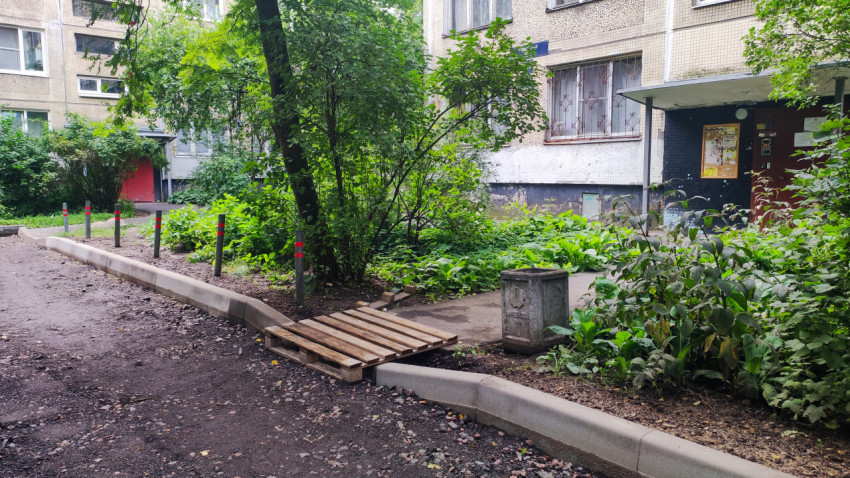 Двор жилого дома с деревянным настилом из поддона у бордюра и входом в подъезд