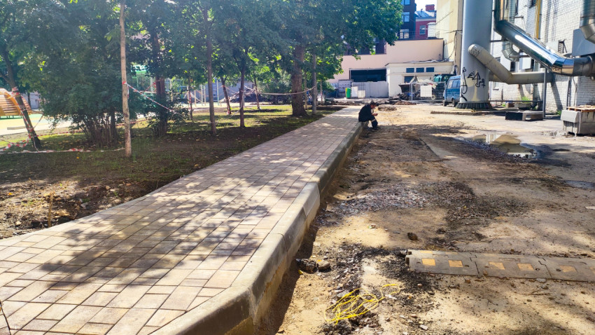 Новый тротуар из плитки с бордюром рядом с грунтовой площадкой и промышленным зданием