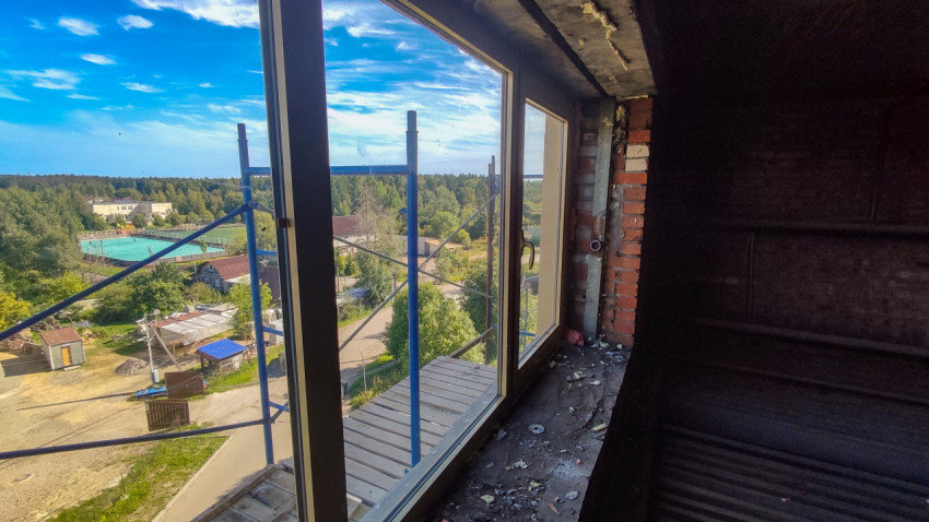 Вид из помещения через пластиковое окно на строительные леса и жилую застройку во время ремонта фасада