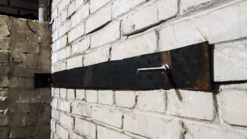 Металлическая анкерная полоса с болтом на белой кирпичной стене в техническом помещении