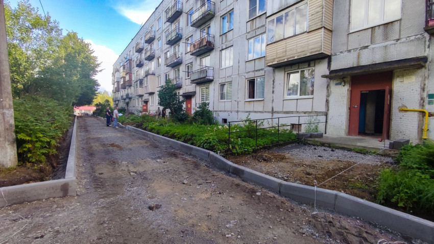 Дворовая дорога с установленными бордюрами вдоль многоэтажного дома и кустарника