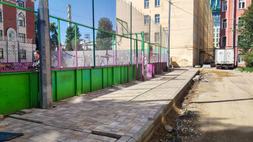 Тротуар из плитки вдоль ограждения спортивной площадки с сеткой и граффити во дворе