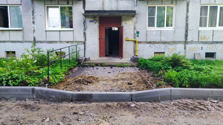 Подъезд с пандусом и ограждённой зоной работ, где готовят основание под дорожку