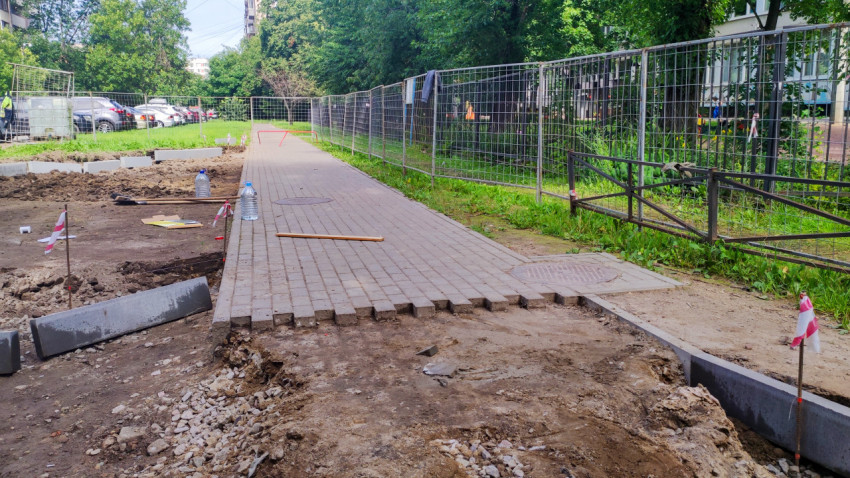 Укладка тротуарной плитки и бордюров на новой пешеходной дорожке за временным ограждением