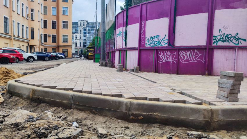 Укладка тротуарной плитки и бордюров на участке двора рядом с ограждением стройки