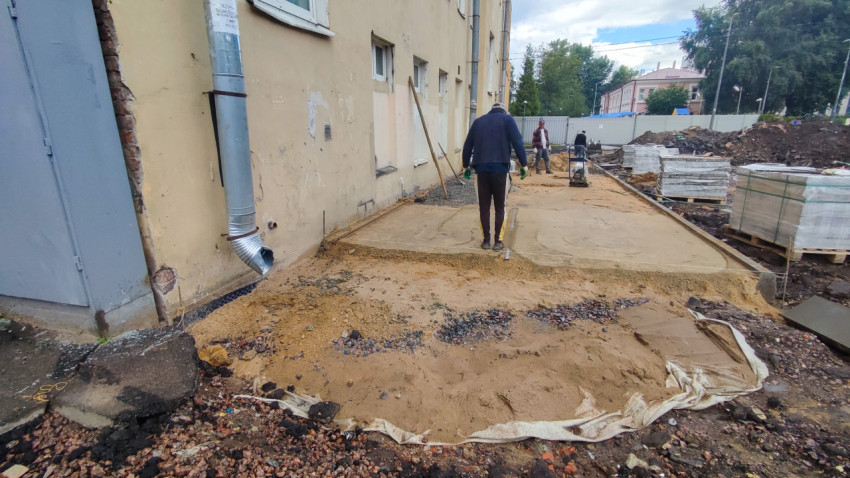 Рабочие укладывают основание из песка и геотекстиля для благоустройства дорожки во дворе