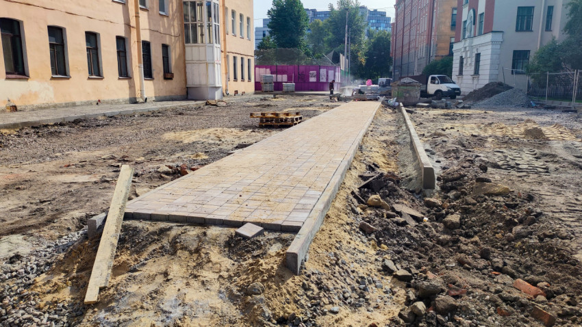 Укладка тротуарной плитки на стройплощадке во дворе с поддонами, грунтом и временным забором