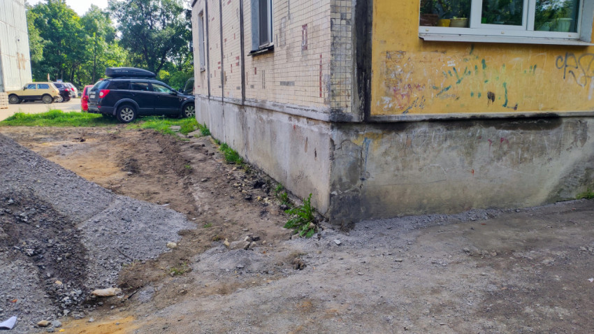 Угловая часть жилого дома с изношенным фасадом, граффити и разрытым грунтом у цоколя