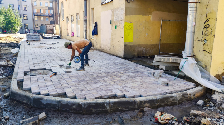 Рабочий режет тротуарную плитку болгаркой при благоустройстве двора у фасада дома