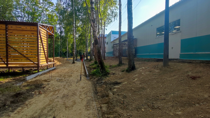 Складирование материалов и подготовка тротуара с бордюром у здания рядом с деревьями