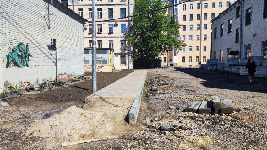 Новая тротуарная дорожка с бордюром и строительными материалами на ремонтируемой дворовой территории