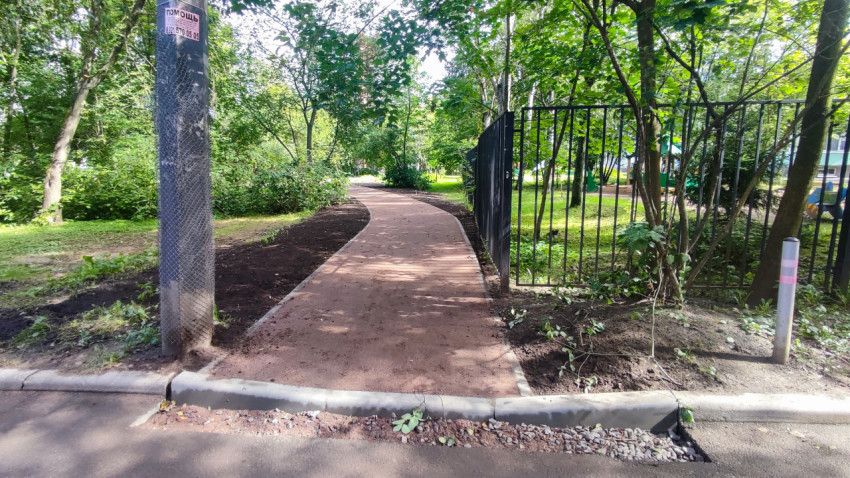 Новая дорожка в городском парке с бордюрами, металлическим ограждением и деревьями