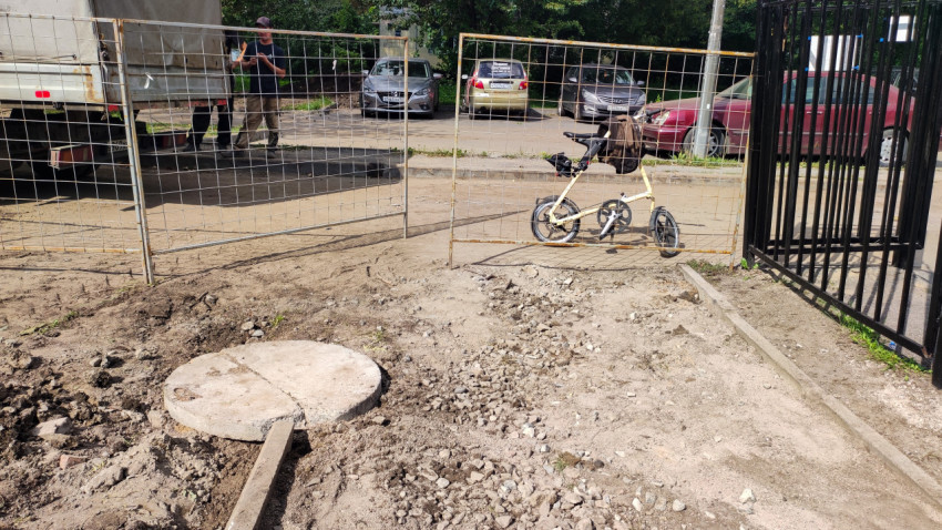 Временное ограждение и люк на земле рядом с дворовым проездом и велосипедом