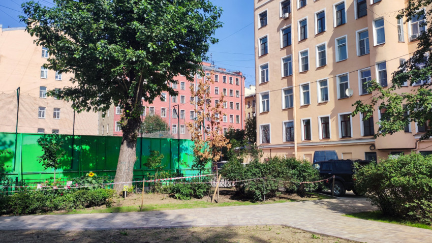 Двор жилых домов с плиточной дорожкой и зелёным ограждением спортивной площадки