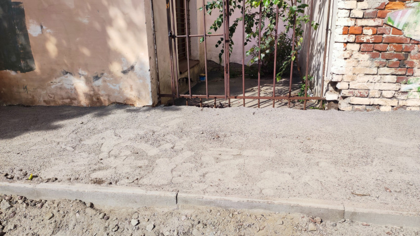 Песчаная подушка и бордюр при ремонте тротуара у цоколя здания и металлической решётки