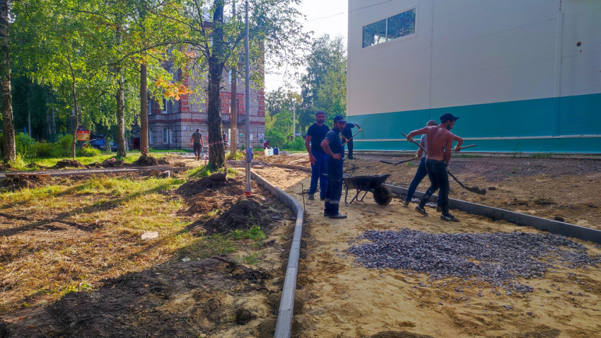 Рабочие выполняют устройство тротуара с бордюром и отсыпкой у здания в зелёной зоне